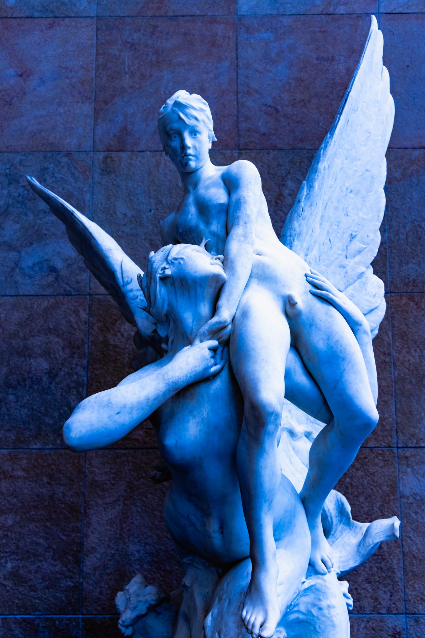 Statue of two winged figures against a textured wall