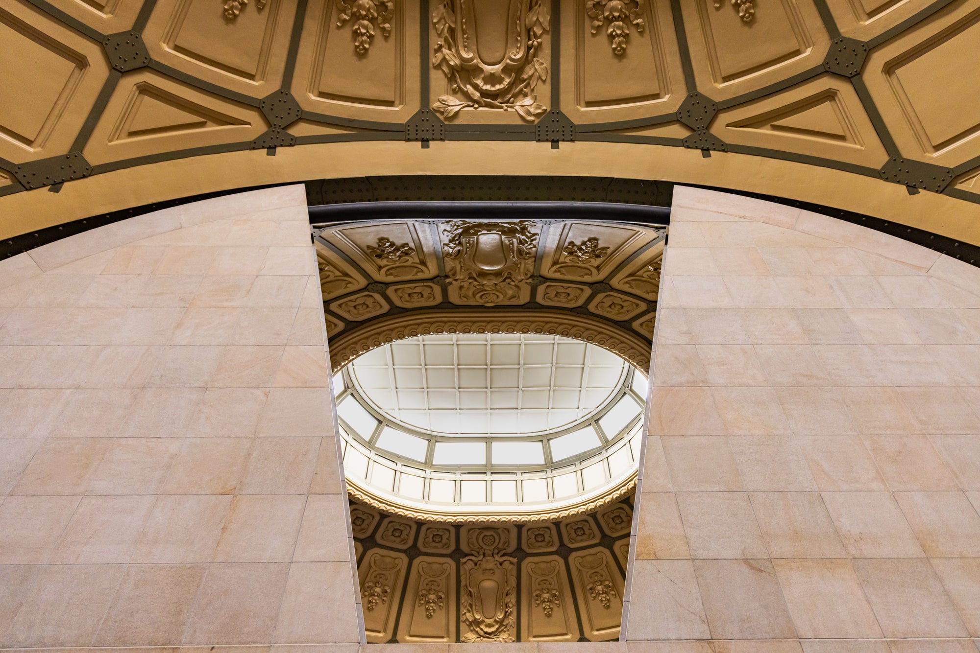 Ornate ceiling with gold accents and a central skylight in a building interior.