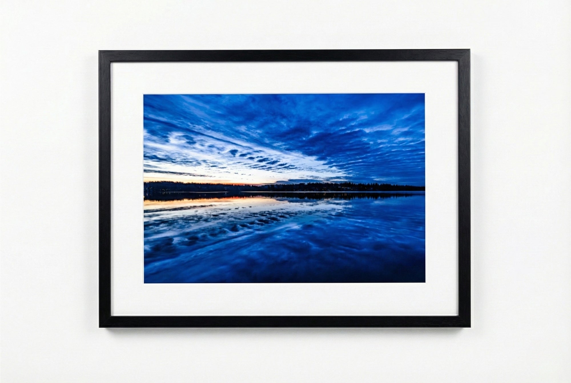 Framed photograph of a blue sky and water landscape on a white wall