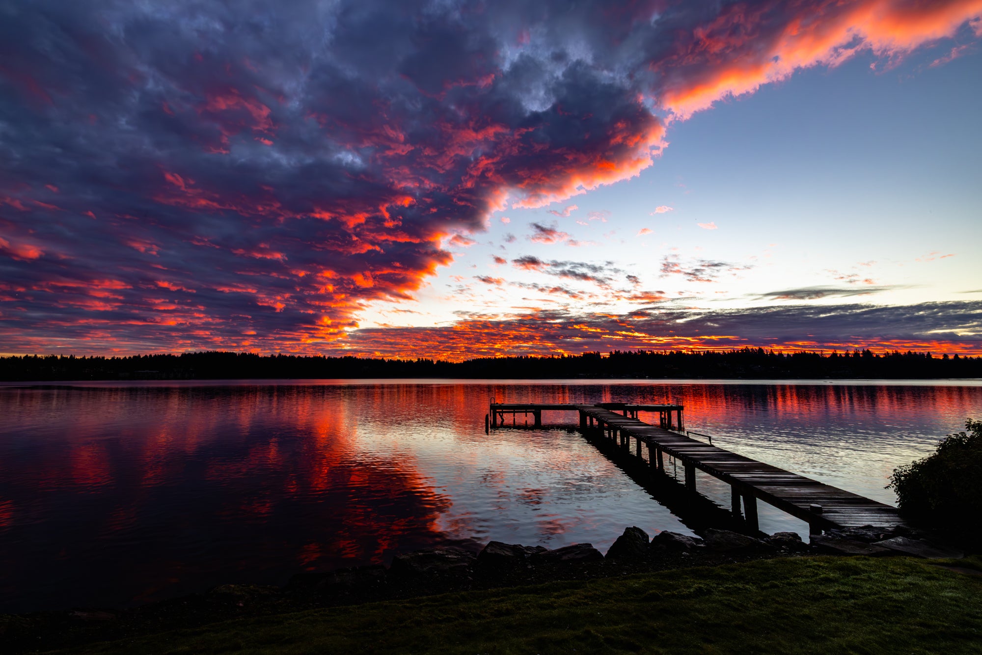 Sunrise over a lake with a dock and colorful clouds.
