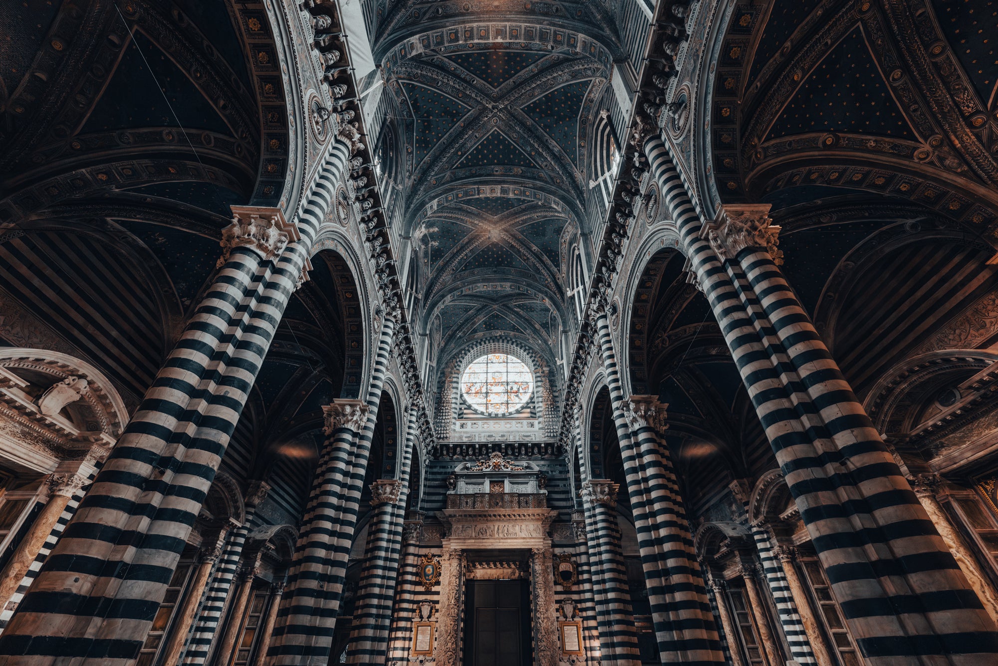Narrow shot of a cathedral interior with striped columns and a large window.
