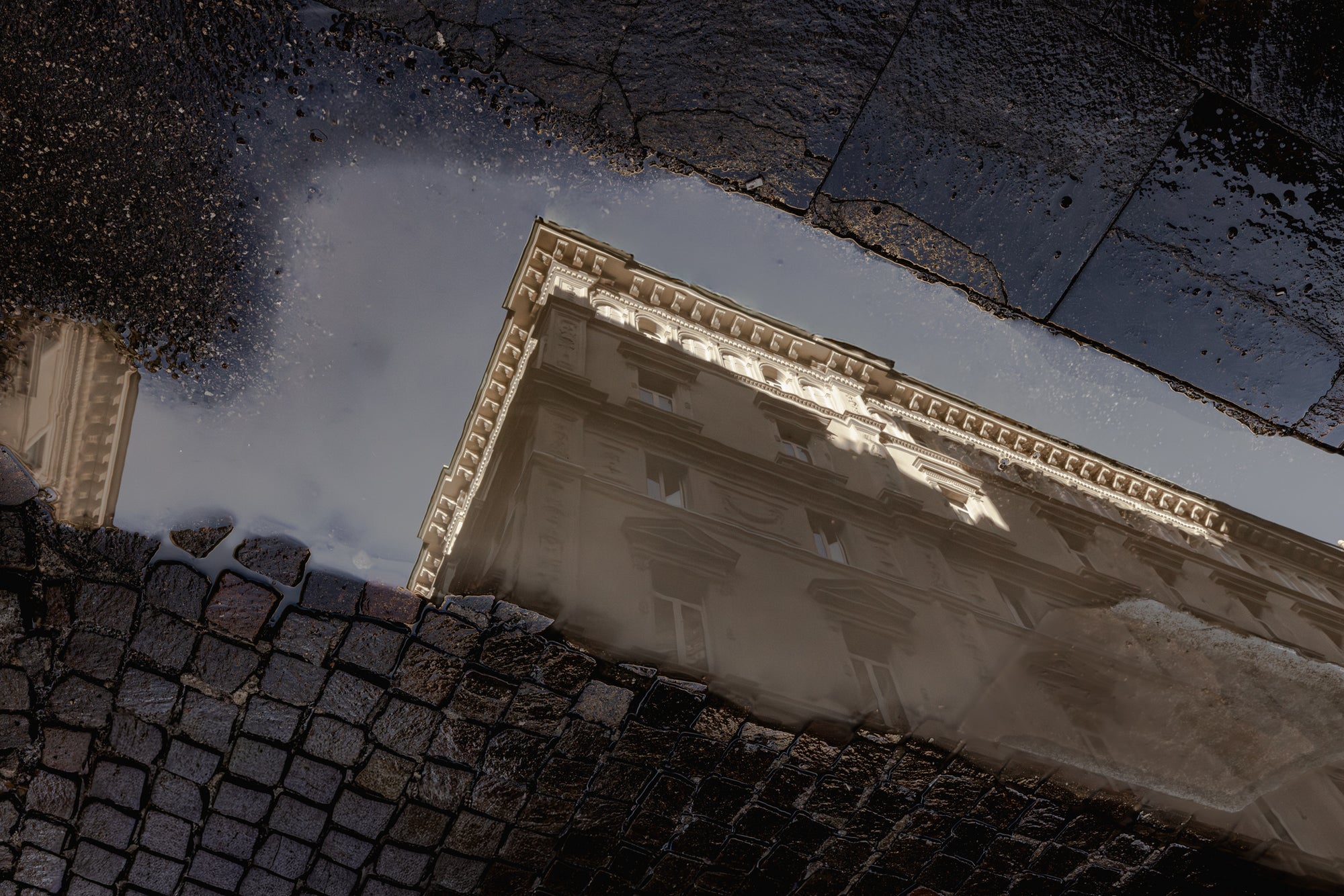 Reflection of a building in a puddle on a cobblestone street