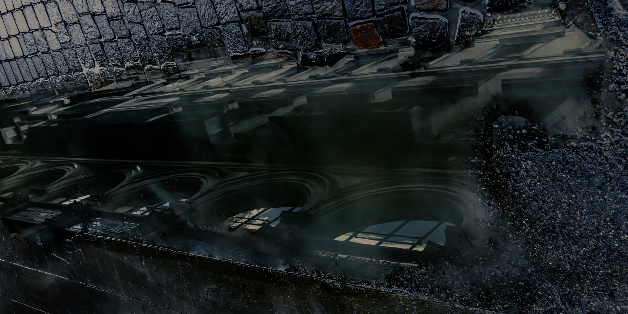 A reflection of a building in a puddle on the cobblestone street.
