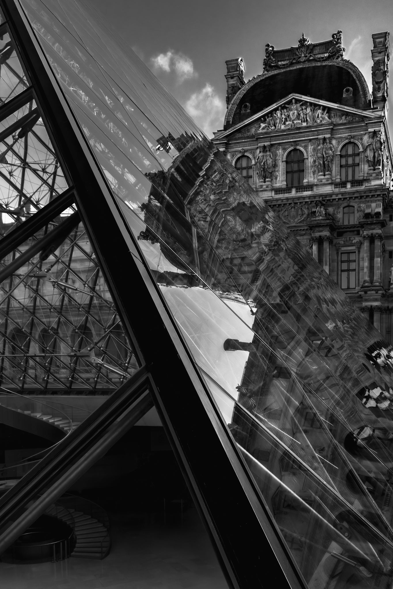 Reflective surface of the Louvre triangle showing a building and sky with clouds.