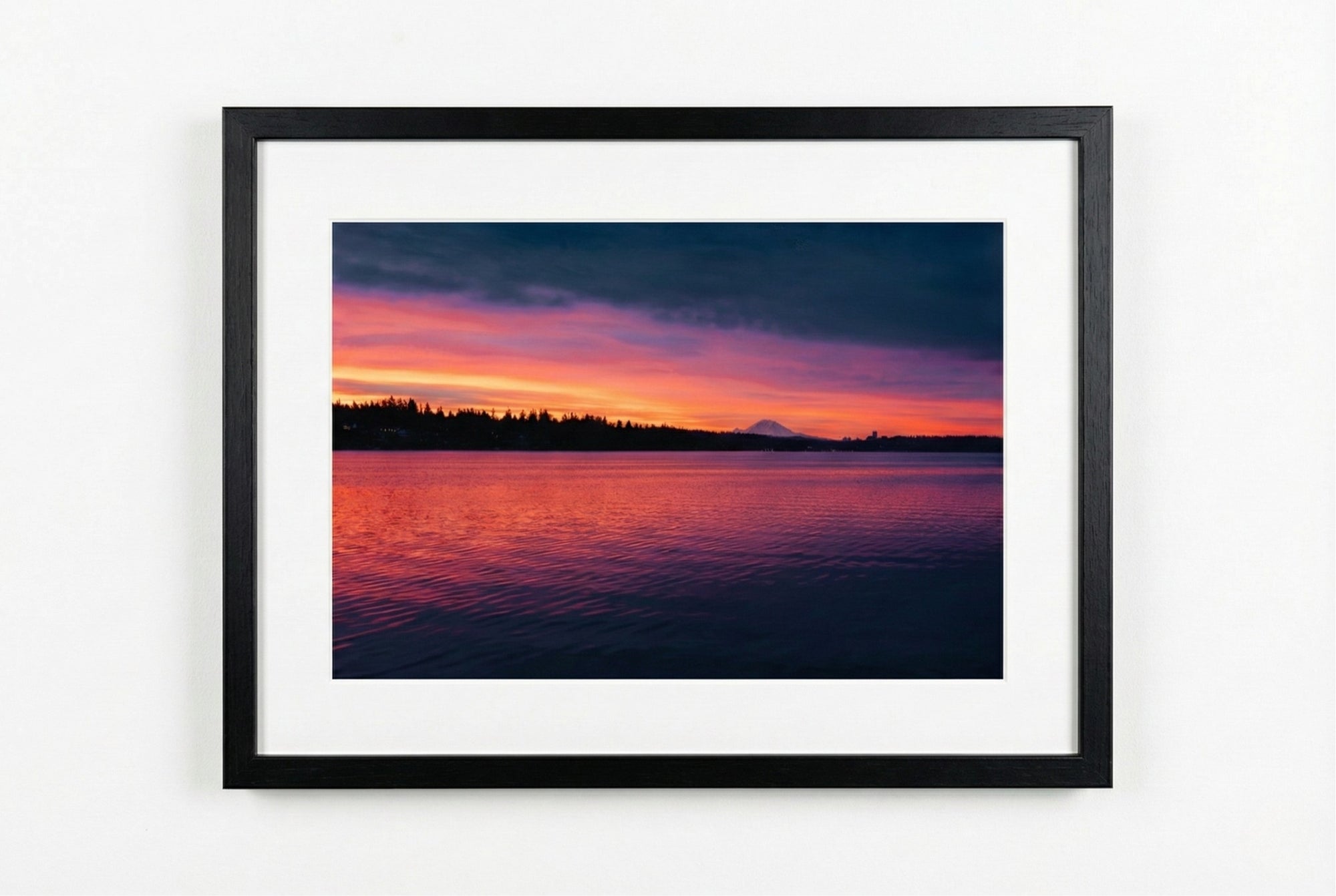 Framed artwork of a sunrise over water with a black frame on a white wall.